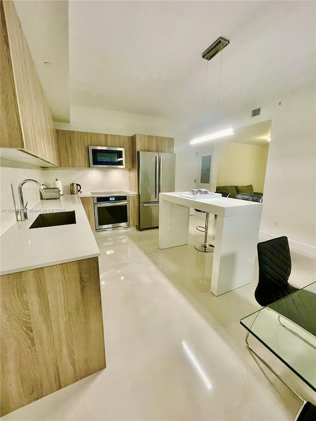 kitchen featuring sink, electric panel, decorative light fixtures, a kitchen bar, and appliances with stainless steel finishes