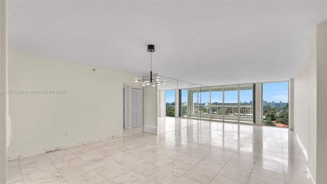 unfurnished room with expansive windows, a notable chandelier, marble finish floor, and baseboards
