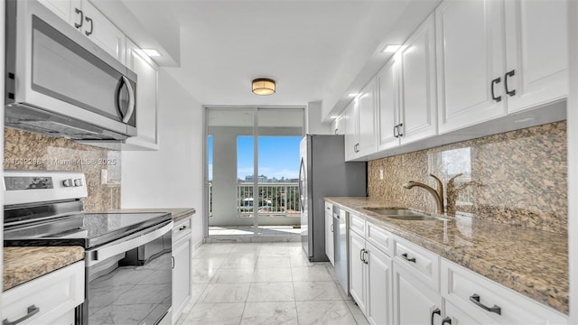 kitchen featuring light stone counters, stainless steel appliances, marble finish floor, a sink, and white cabinetry