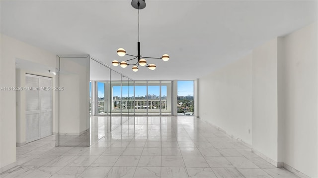 empty room with an inviting chandelier, a wall of windows, marble finish floor, and baseboards