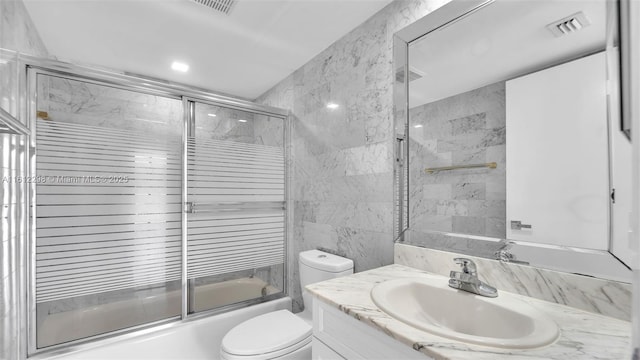 bathroom featuring tile walls, vanity, toilet, visible vents, and enclosed tub / shower combo