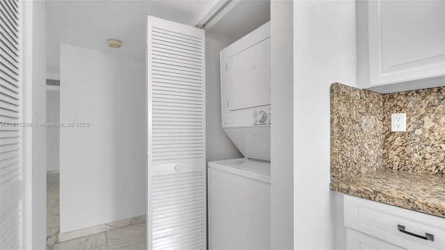 laundry area featuring marble finish floor, stacked washer and clothes dryer, laundry area, and baseboards