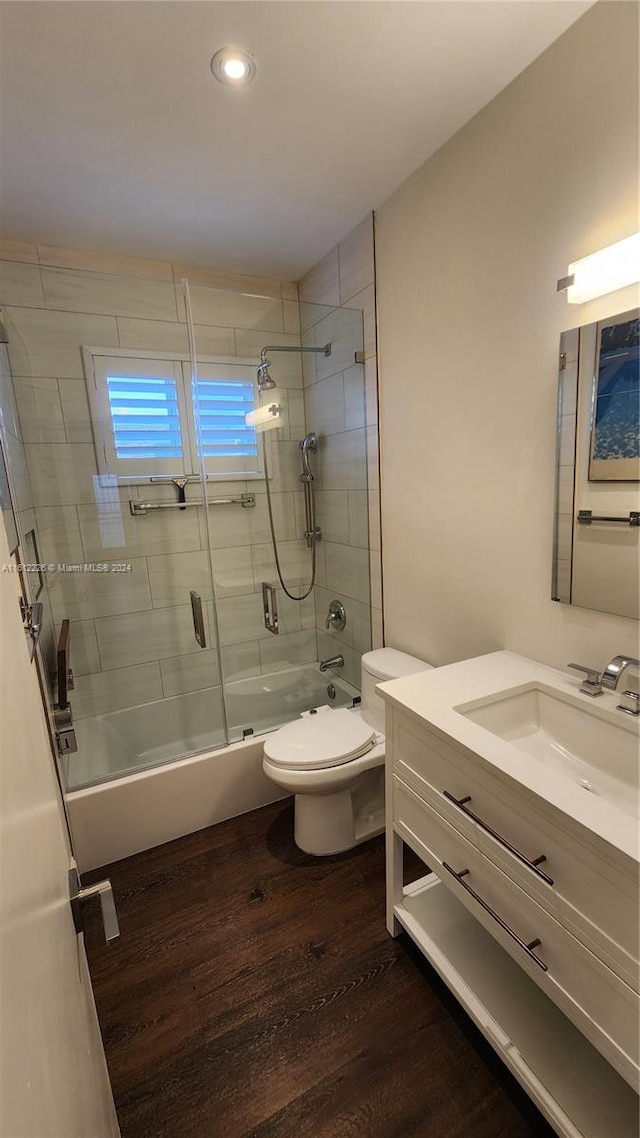 full bathroom featuring vanity, wood-type flooring, toilet, and bath / shower combo with glass door