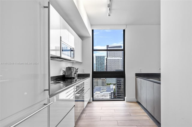 kitchen with rail lighting, wall oven, light hardwood / wood-style floors, and white cabinetry