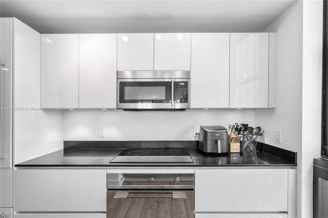 kitchen featuring white cabinets, hardwood / wood-style flooring, stainless steel appliances, and dark stone counters