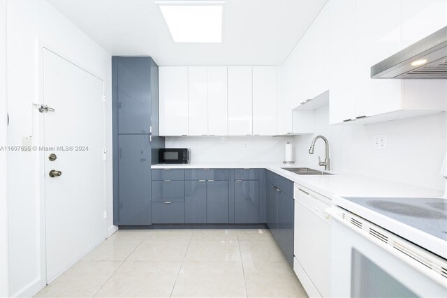 kitchen featuring stove, white dishwasher, light tile floors, wall chimney range hood, and white cabinetry