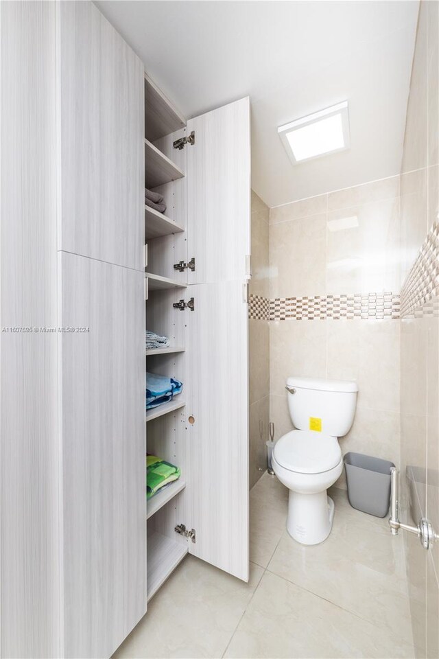 bathroom with tile flooring, toilet, and tile walls