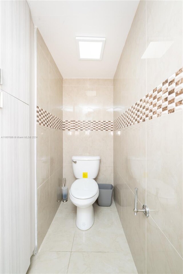 bathroom with walk in shower, tile flooring, toilet, and tile walls