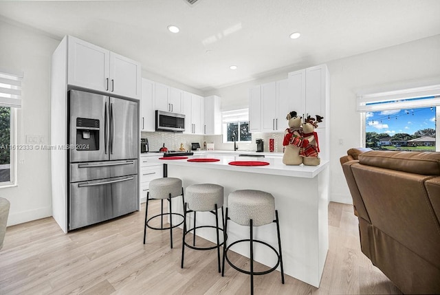 kitchen with a kitchen bar, appliances with stainless steel finishes, a wealth of natural light, light hardwood / wood-style flooring, and white cabinets