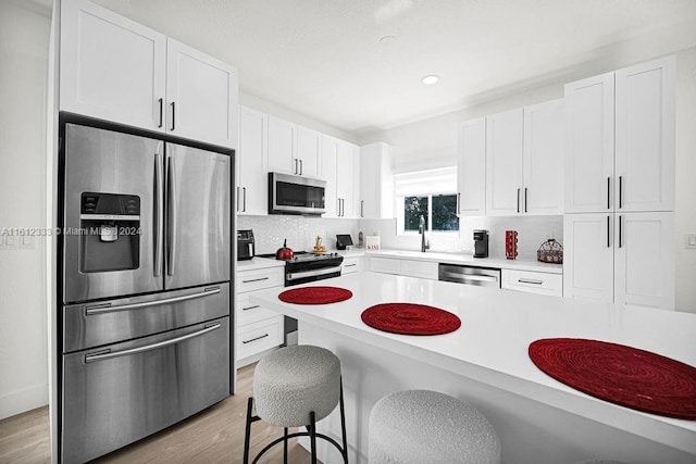 kitchen featuring white cabinetry, stainless steel appliances, a breakfast bar area, and light hardwood / wood-style flooring