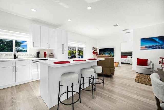 kitchen with dishwasher, a center island, a kitchen breakfast bar, sink, and white cabinetry