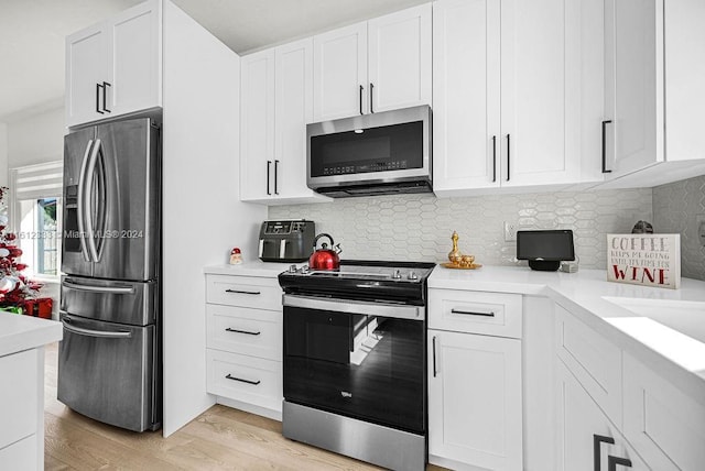 kitchen with white cabinets, appliances with stainless steel finishes, backsplash, and light hardwood / wood-style flooring