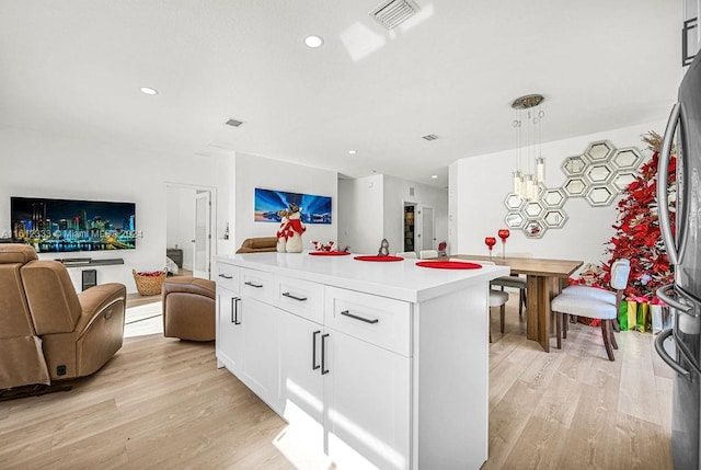 kitchen featuring a center island, white cabinets, hanging light fixtures, stainless steel fridge, and light hardwood / wood-style floors