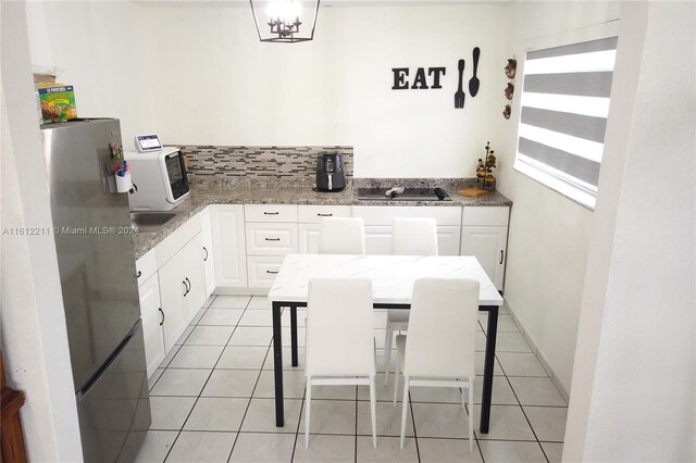 kitchen with light stone counters, white cabinets, stainless steel fridge, and light tile floors