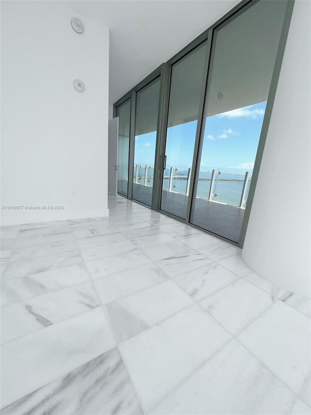 unfurnished room featuring floor to ceiling windows, a water view, and light tile floors