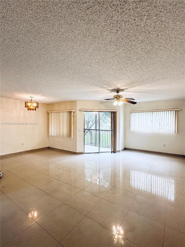 unfurnished room featuring a wealth of natural light and ceiling fan with notable chandelier