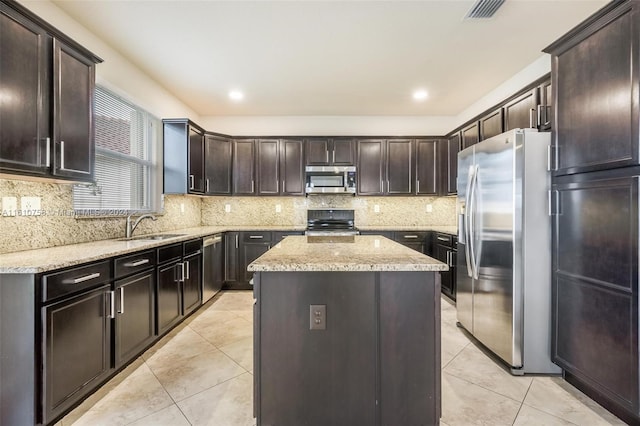 kitchen with light stone countertops, appliances with stainless steel finishes, dark brown cabinets, sink, and a center island