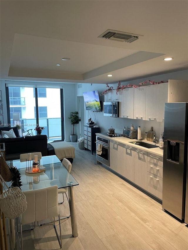 kitchen featuring appliances with stainless steel finishes, sink, a raised ceiling, and light hardwood / wood-style flooring