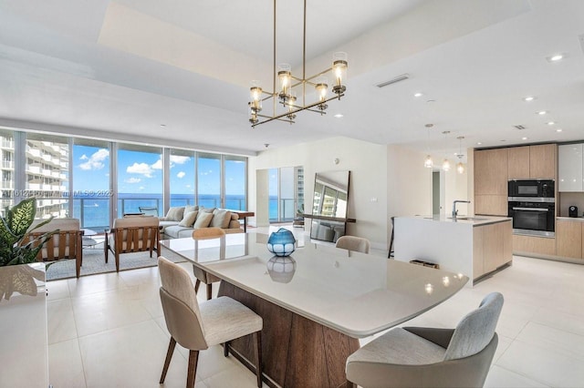 tiled dining area with floor to ceiling windows, sink, a chandelier, a tray ceiling, and a water view