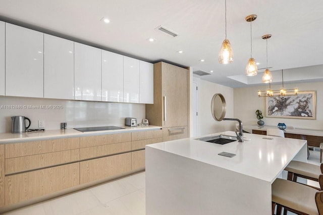 kitchen with white cabinetry, light brown cabinets, sink, decorative light fixtures, and black electric cooktop