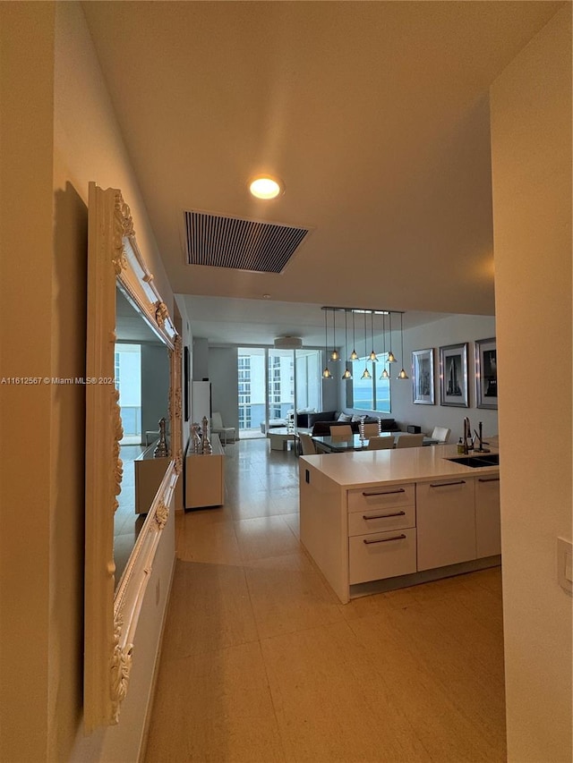 kitchen with white cabinets, sink, light tile floors, and pendant lighting