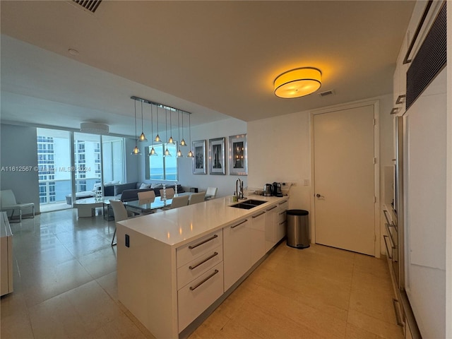 kitchen with kitchen peninsula, decorative light fixtures, light tile flooring, sink, and white cabinetry