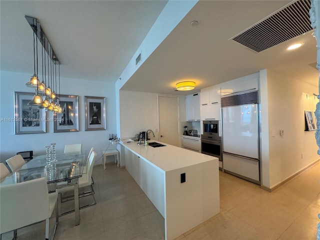 kitchen with oven, built in fridge, white cabinetry, a peninsula, and visible vents
