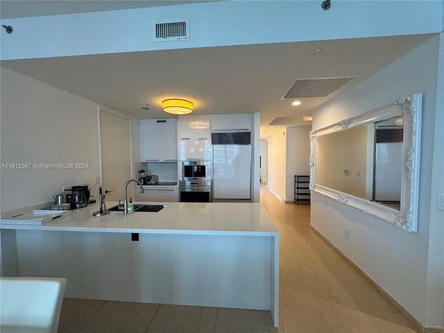 kitchen with kitchen peninsula, fridge, white cabinets, sink, and light tile floors