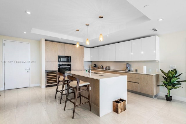 kitchen featuring a kitchen island with sink, a raised ceiling, white cabinetry, and hanging light fixtures