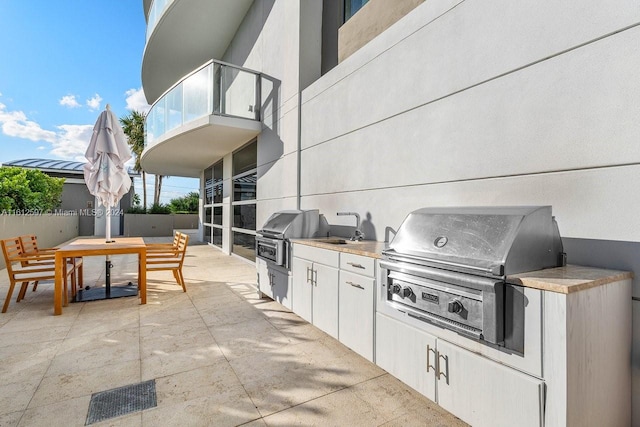 view of patio with grilling area, a balcony, an outdoor kitchen, and sink