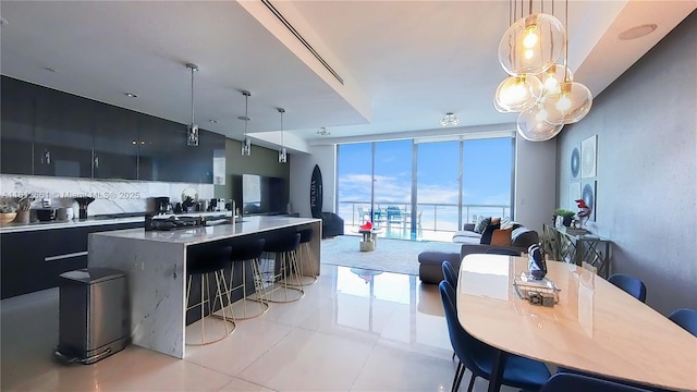 kitchen featuring decorative light fixtures, an island with sink, light tile patterned floors, tasteful backsplash, and a wall of windows