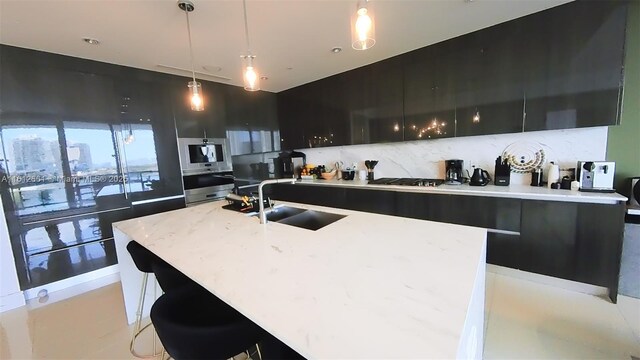 kitchen featuring sink, pendant lighting, an island with sink, and tasteful backsplash