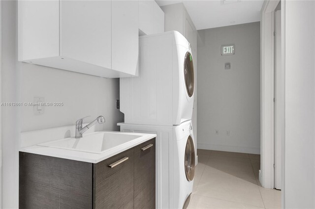 clothes washing area featuring sink, cabinets, stacked washing maching and dryer, and light tile patterned flooring