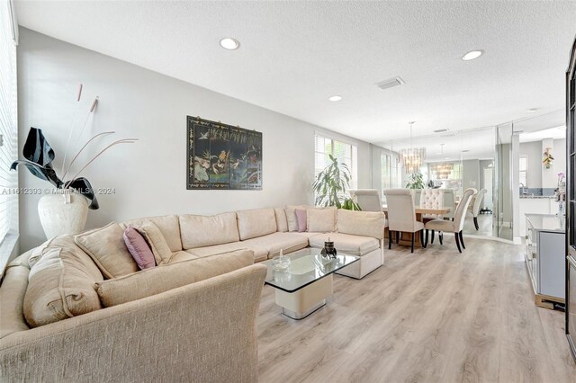 living room featuring a notable chandelier, light hardwood / wood-style flooring, and a textured ceiling