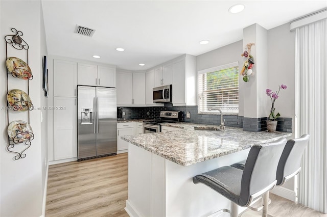 kitchen with light hardwood / wood-style floors, kitchen peninsula, stainless steel appliances, tasteful backsplash, and sink