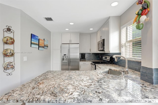 kitchen featuring appliances with stainless steel finishes, white cabinets, light stone counters, backsplash, and sink