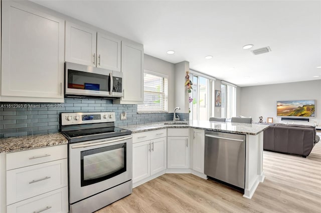 kitchen featuring white cabinets, light hardwood / wood-style flooring, light stone countertops, and stainless steel appliances