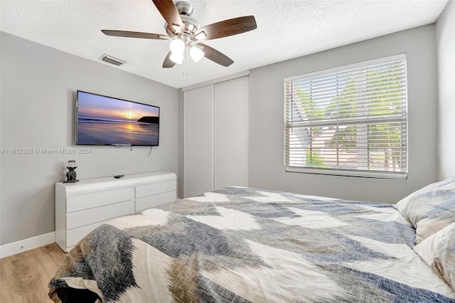 bedroom featuring light hardwood / wood-style floors, a textured ceiling, a closet, and ceiling fan