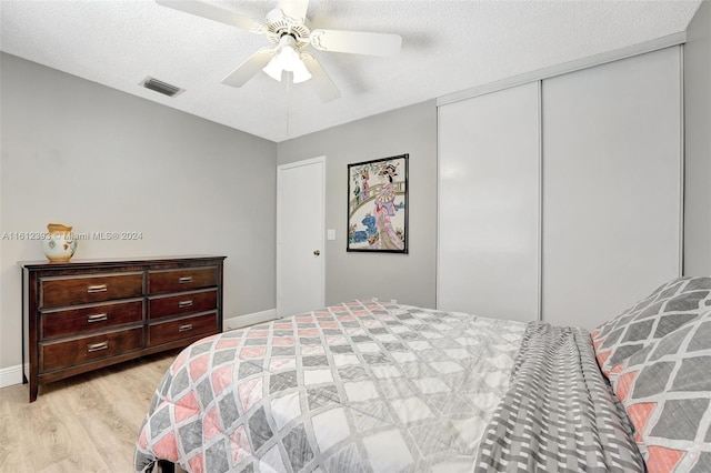 bedroom with a textured ceiling, a closet, ceiling fan, and light wood-type flooring