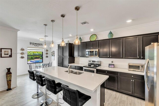 kitchen with a center island with sink, light wood-type flooring, appliances with stainless steel finishes, sink, and pendant lighting