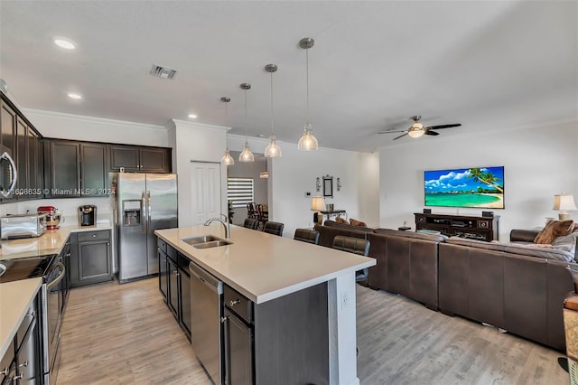 kitchen featuring stainless steel appliances, a sink, open floor plan, light countertops, and a center island with sink