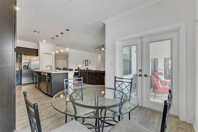 dining area featuring ceiling fan, crown molding, light wood-type flooring, sink, and french doors