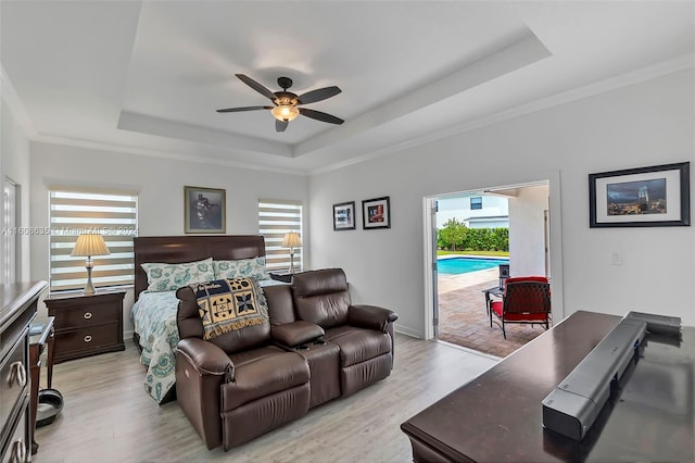 bedroom with access to exterior, a raised ceiling, crown molding, and light wood-style flooring