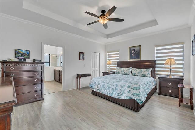 bedroom featuring a tray ceiling, ensuite bathroom, multiple windows, and ceiling fan