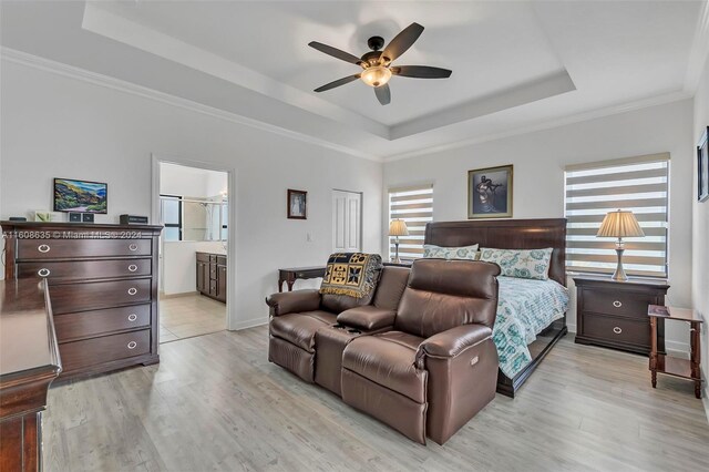 bedroom featuring crown molding, light wood-type flooring, ensuite bathroom, ceiling fan, and a raised ceiling