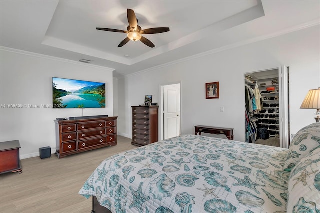 bedroom featuring ceiling fan, a walk in closet, a tray ceiling, and light wood-type flooring