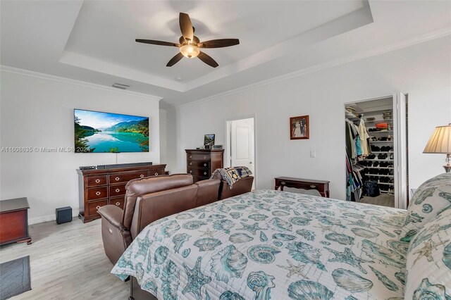 bedroom with a closet, ceiling fan, a tray ceiling, and light hardwood / wood-style flooring