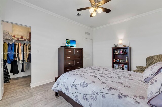 bedroom featuring ceiling fan, a closet, light hardwood / wood-style floors, crown molding, and a spacious closet