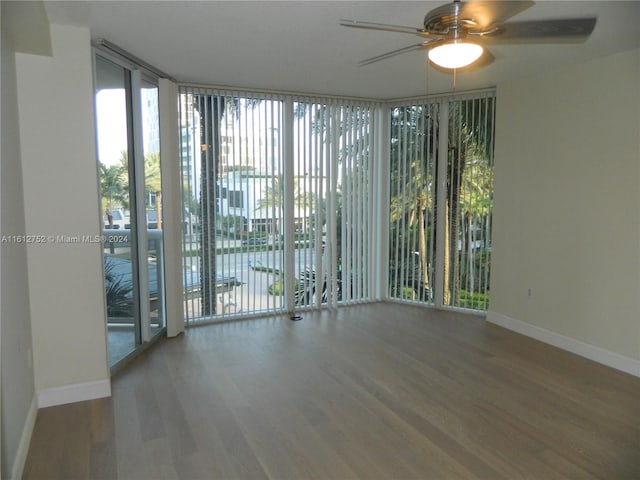 empty room featuring floor to ceiling windows, wood-type flooring, ceiling fan, and a healthy amount of sunlight