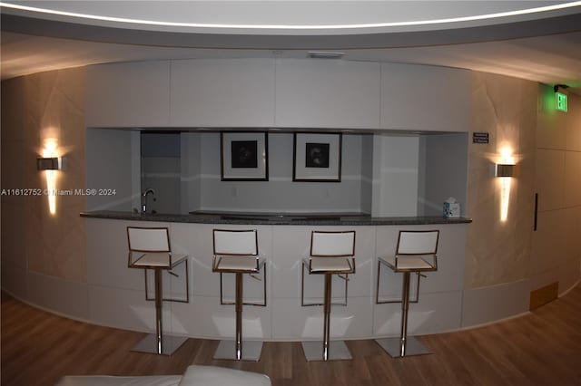 kitchen featuring white cabinetry, wood-type flooring, a breakfast bar area, and sink